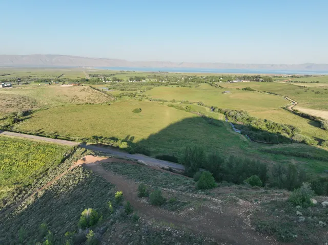 Expansive green landscape featuring a distant body of water, rolling hills, a meandering stream, and scattered trees