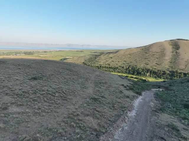 Expansive land featuring a natural terrain, distant lake, and rolling hills