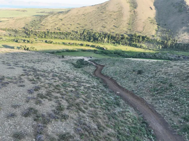 Winding dirt road traversing rolling, brush-covered terrain