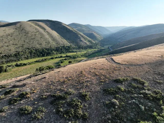 Expansive mountain landscape featuring a winding valley and a visible path across the hillside