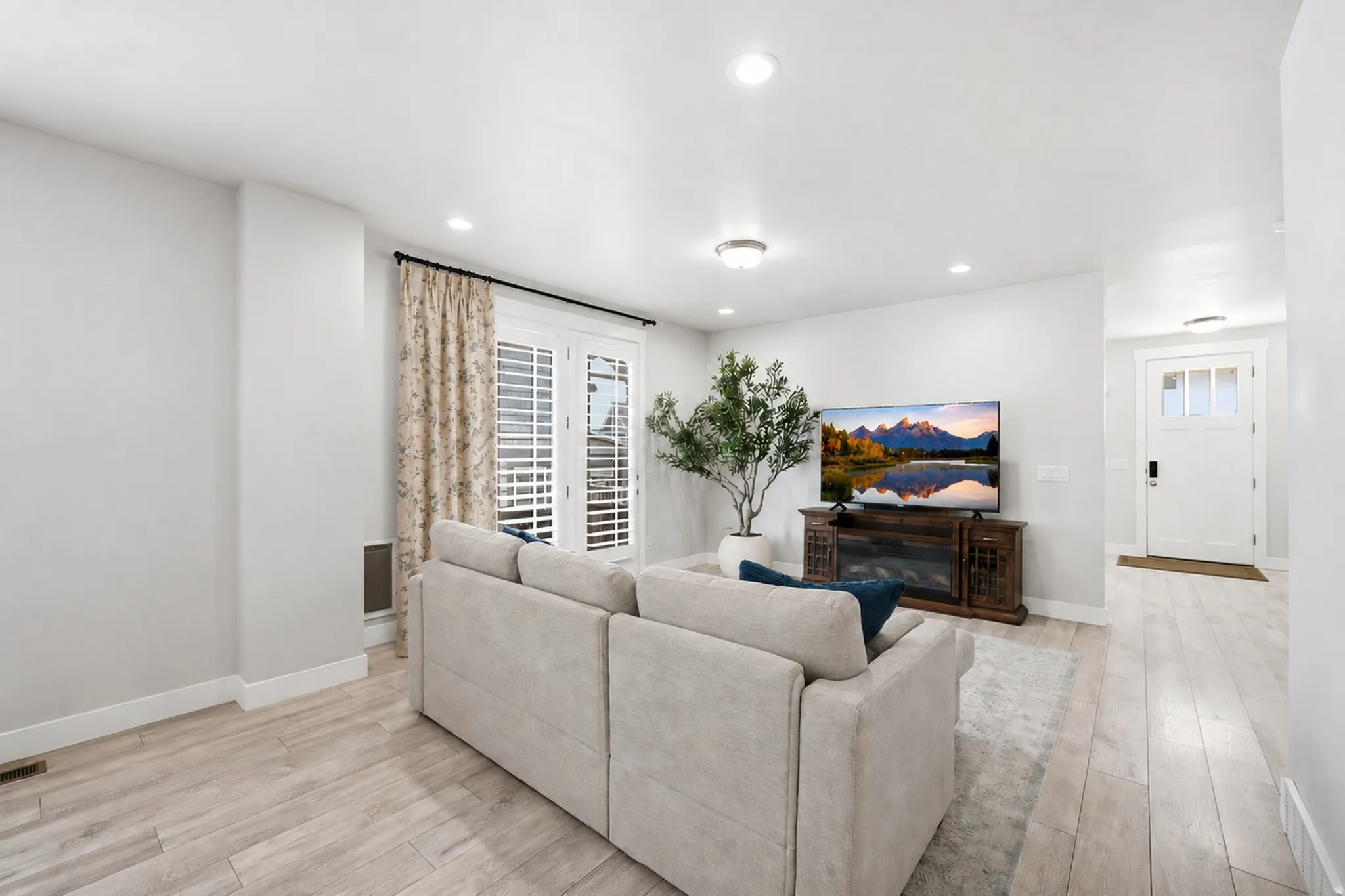 Living area featuring light wood-finish flooring, recessed lighting, and a white paneled door with louvered shutters