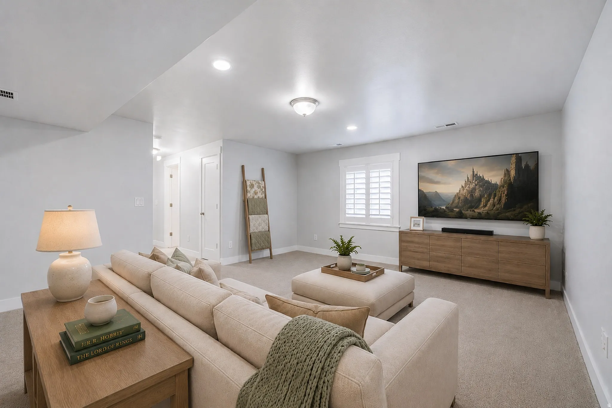 Spacious living area featuring neutral carpeting, recessed lighting, white window shutters, and a wood-finish media console
