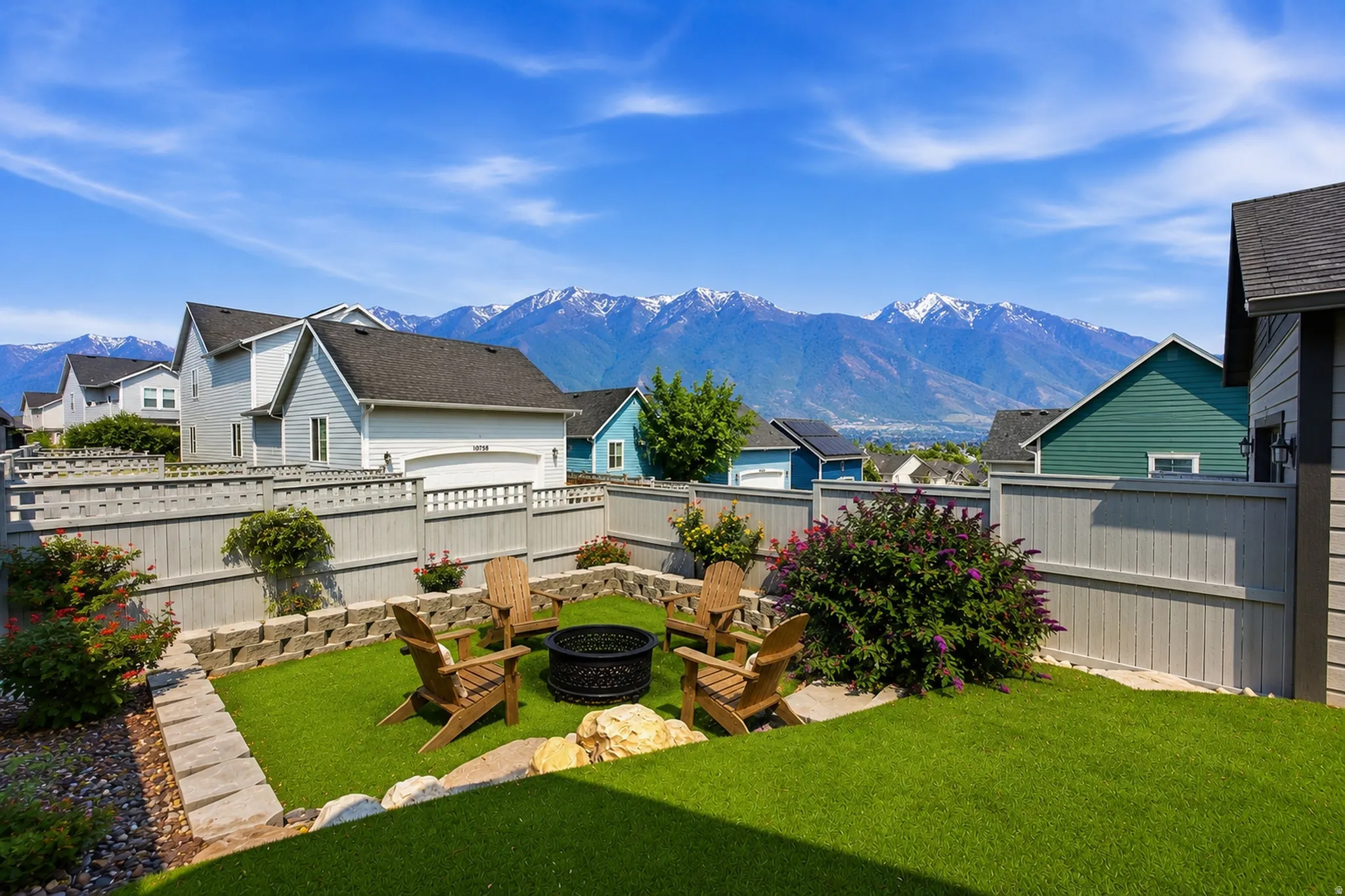 Landscaped backyard featuring a built-in fire pit, artificial turf, retaining walls, and a perimeter fence