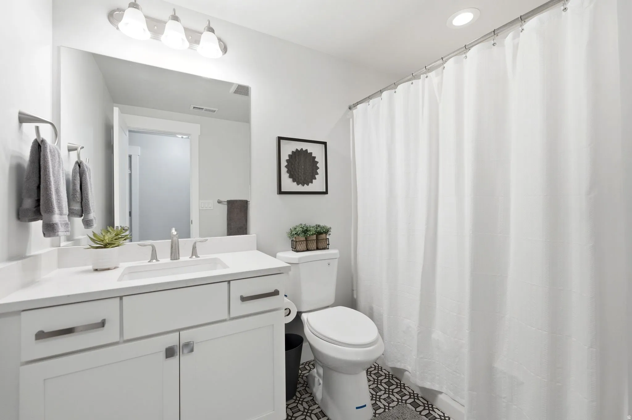 Bathroom featuring a white vanity with an integrated sink and brushed nickel faucet, a large rectangular mirror, and a three-light fixture overhead