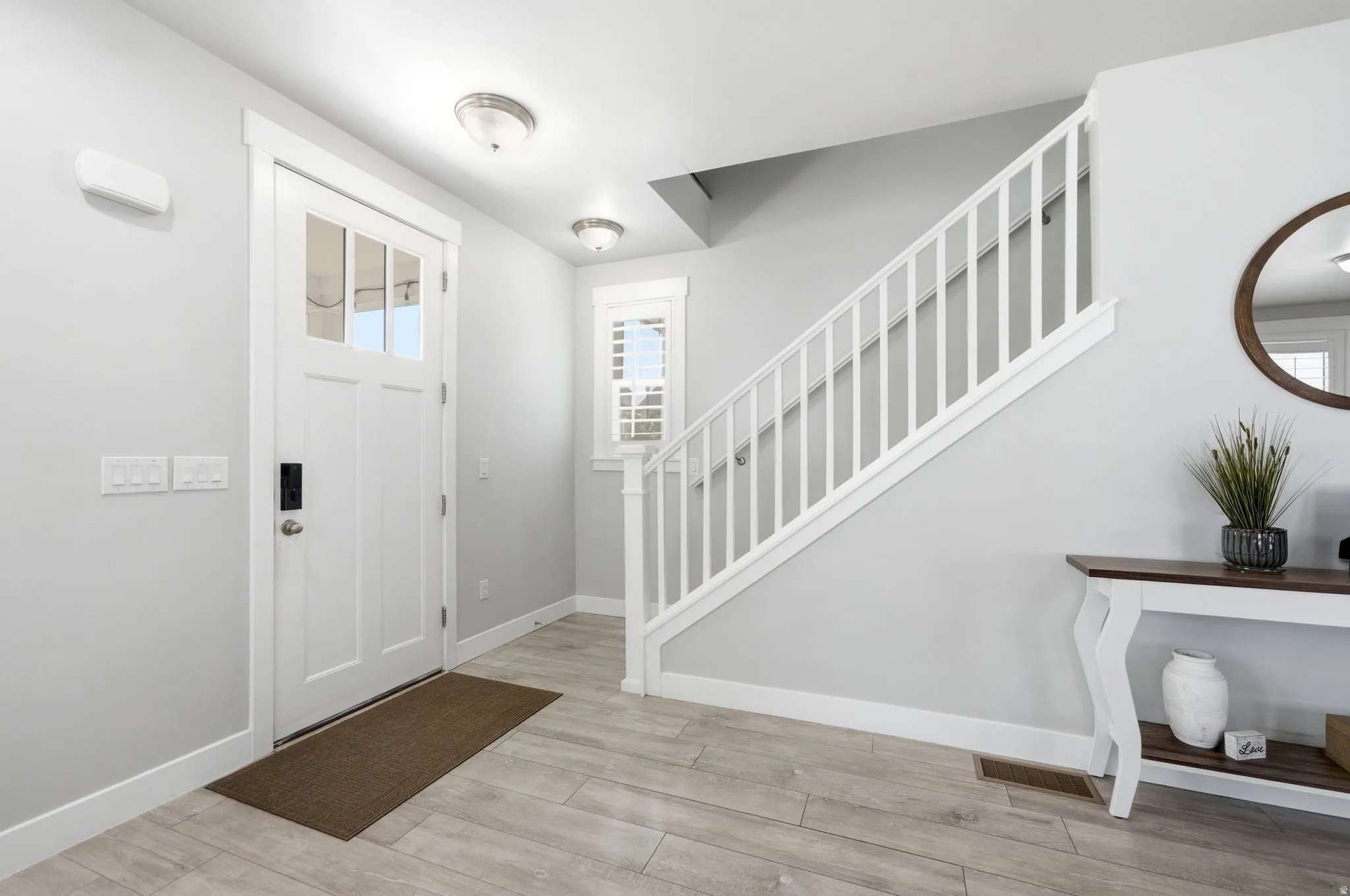 Entryway featuring a white paneled door with glass inserts, light wood-finish flooring, a white staircase with balusters and handrail, a window with white louvered shutters, and recessed ceiling lighting