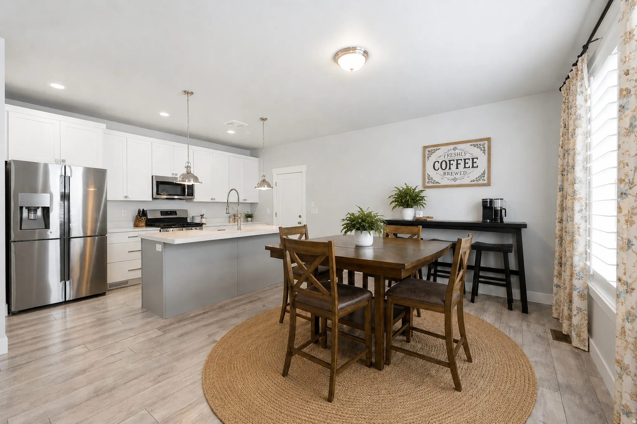 Open-concept kitchen and dining area featuring light wood-finish flooring, white cabinetry, stainless steel appliances, a center island with a light-colored countertop, and recessed lighting