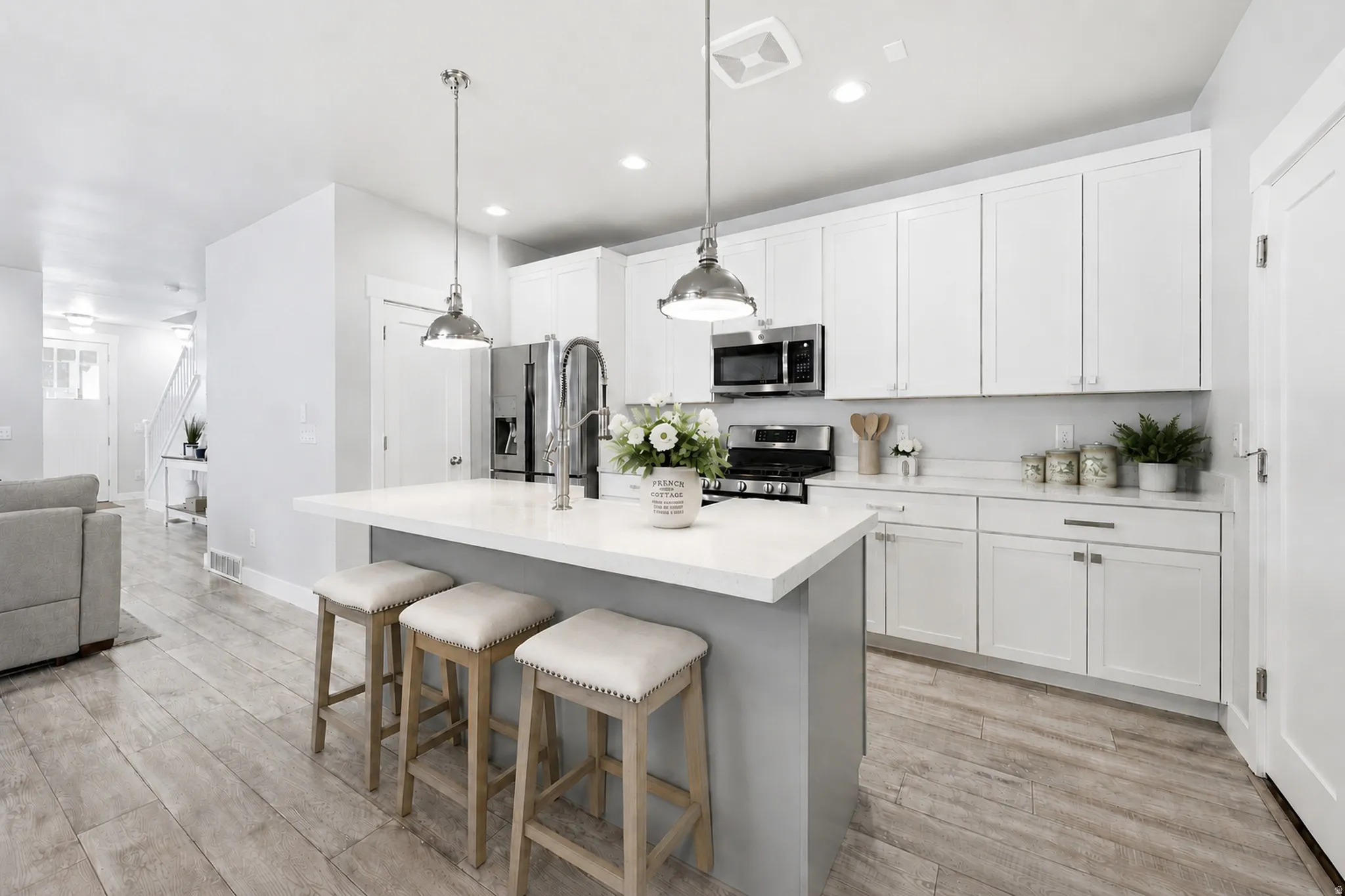 Kitchen featuring an island with a light-colored countertop, stainless steel appliances, light-toned wood-finish flooring, white cabinetry, and recessed lighting