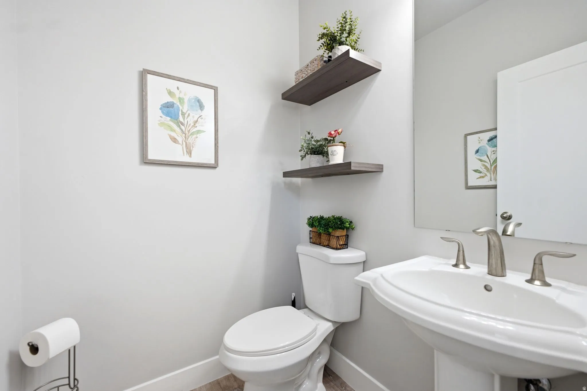 Pedestal sink with brushed nickel faucet, wall-mounted mirror, and wood-finish floating shelves