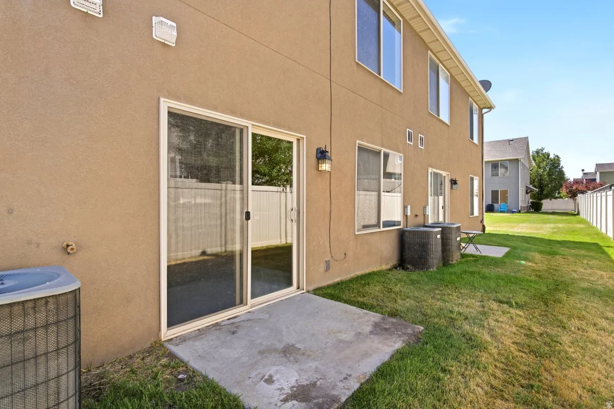 Rear exterior featuring a sliding glass door, a concrete patio, a stucco facade, a fenced yard, and multiple window openings