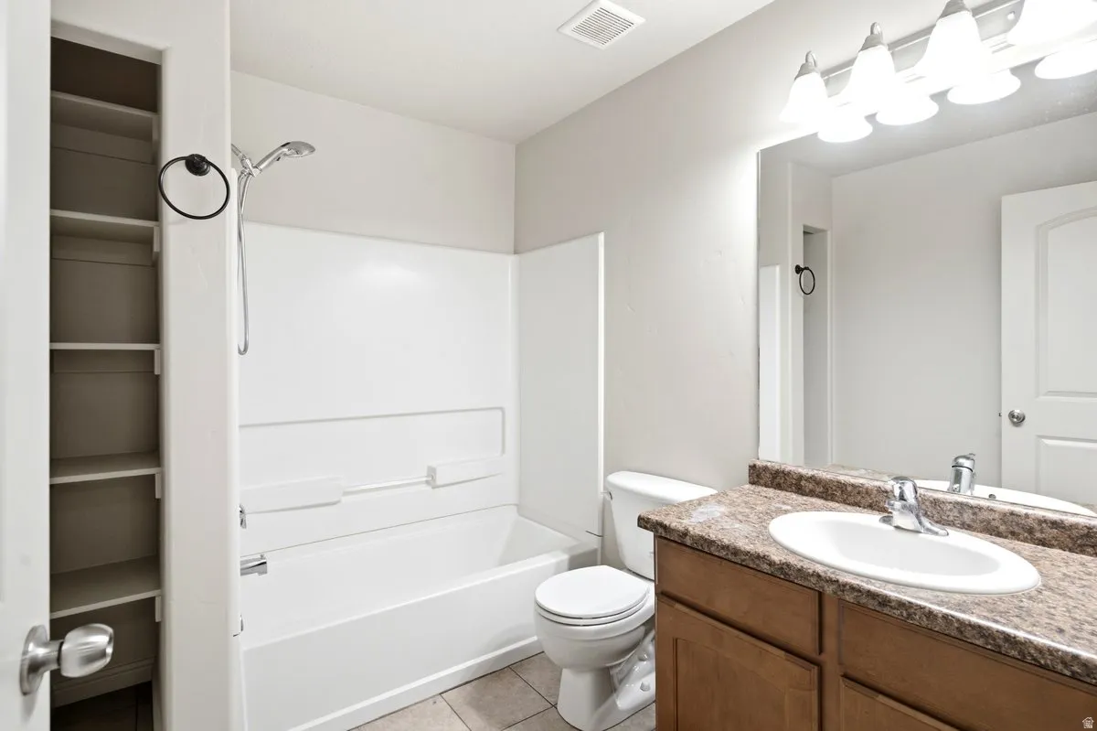 Bathroom featuring a white bathtub and shower surround, a built-in linen closet with shelving, a vanity with a speckled countertop, an undermount sink, and a chrome faucet