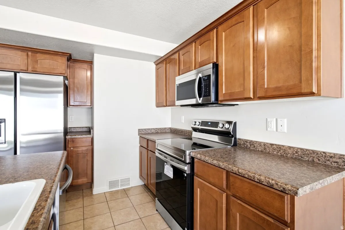 Kitchen featuring stainless steel appliances, wood cabinetry, stone-finish countertops, and tile flooring