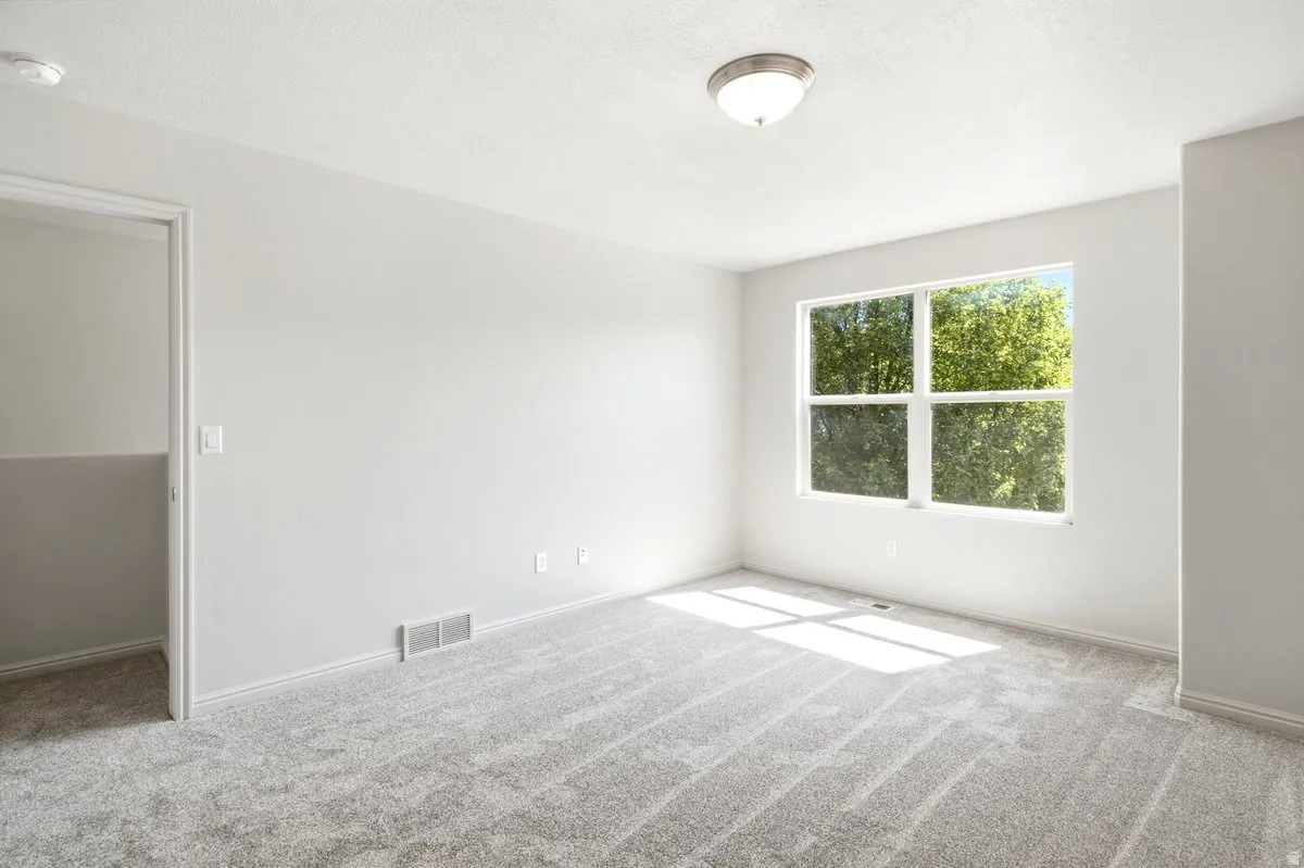 Spacious room featuring light gray carpeting, neutral wall paint, and a multi-pane window