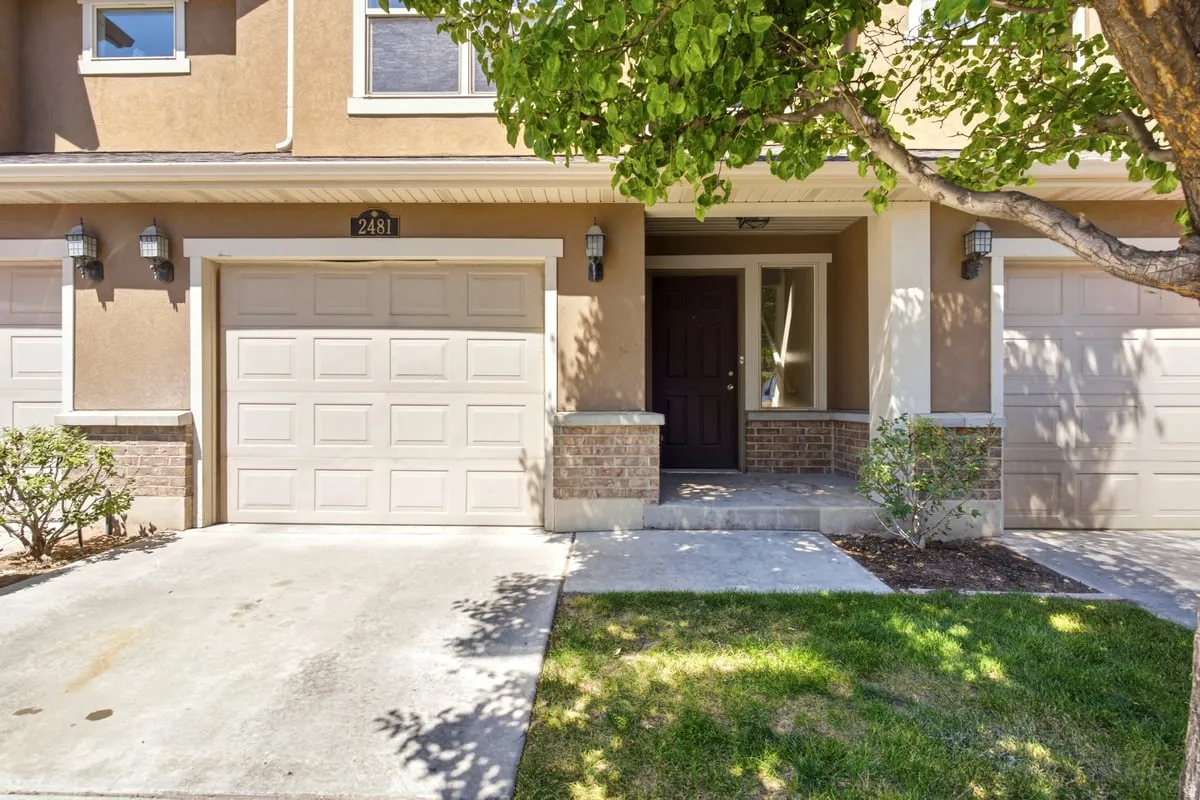 Stucco facade featuring a central entry with a dark-paneled door, two panel-style garage doors, and brick detailing
