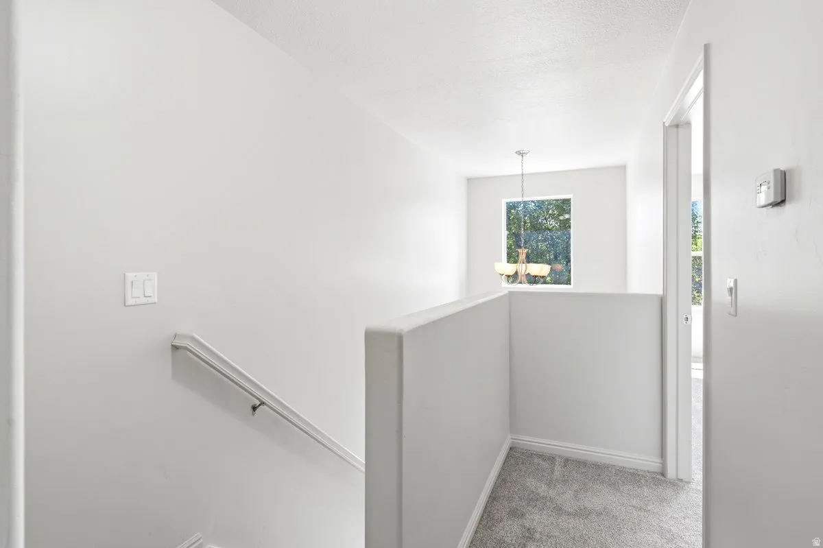 Upper-level landing featuring light gray carpeting, white painted walls, a simple white handrail, and a window with a suspended light fixture