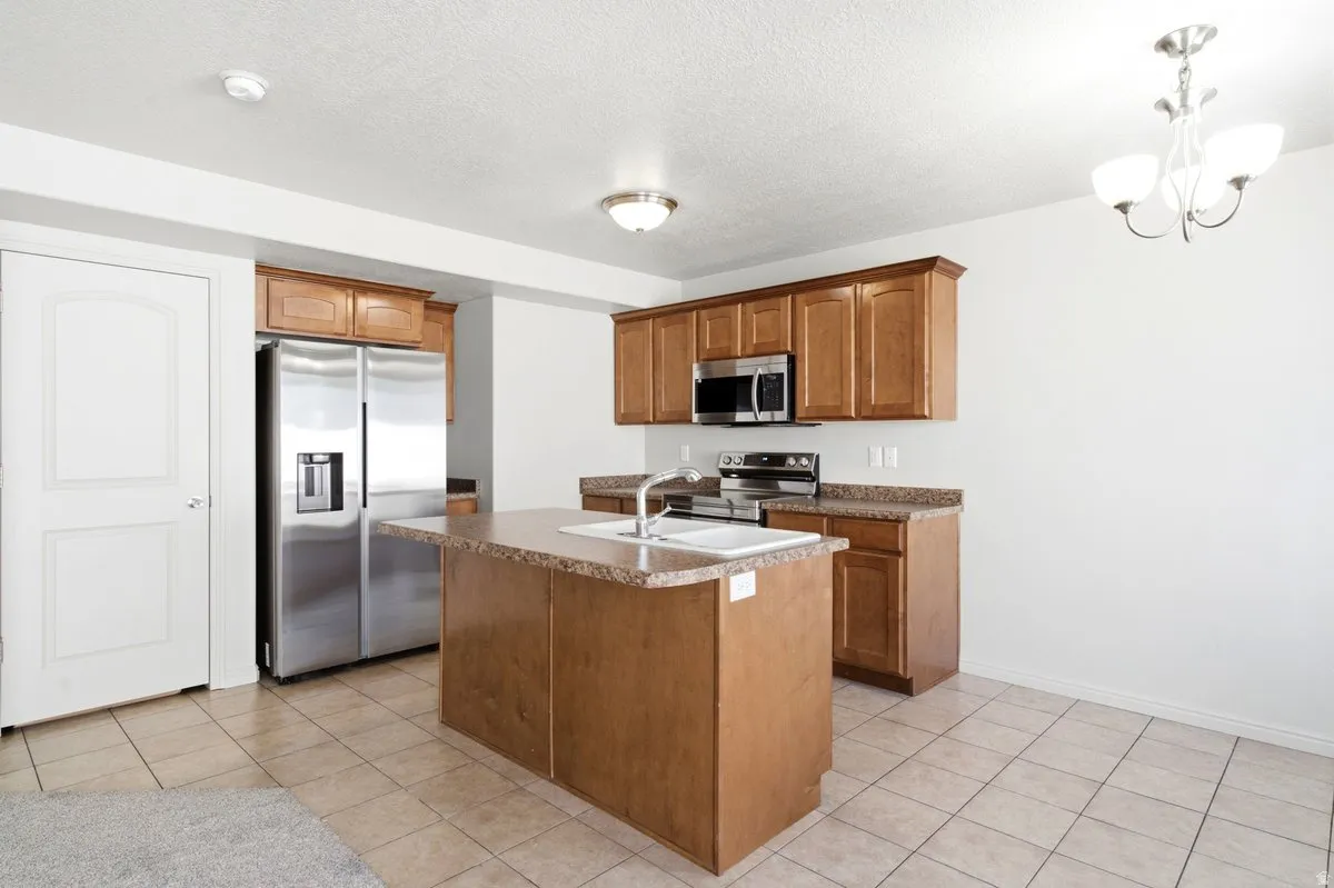 Kitchen featuring a central island with a built-in sink, wood-finish cabinetry, stainless steel appliances, and tile flooring