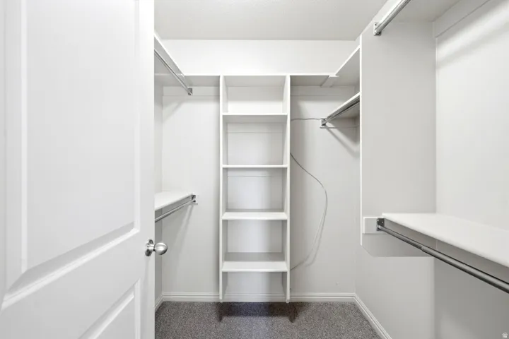 Walk-in closet featuring built-in shelving, multiple hanging rods, white trim, and light grey carpeting