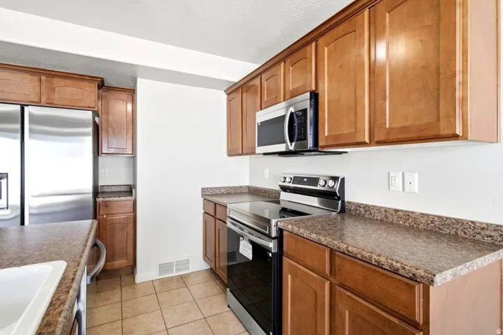 Kitchen featuring stainless steel appliances, wood cabinetry, stone-finish countertops, and tile flooring
