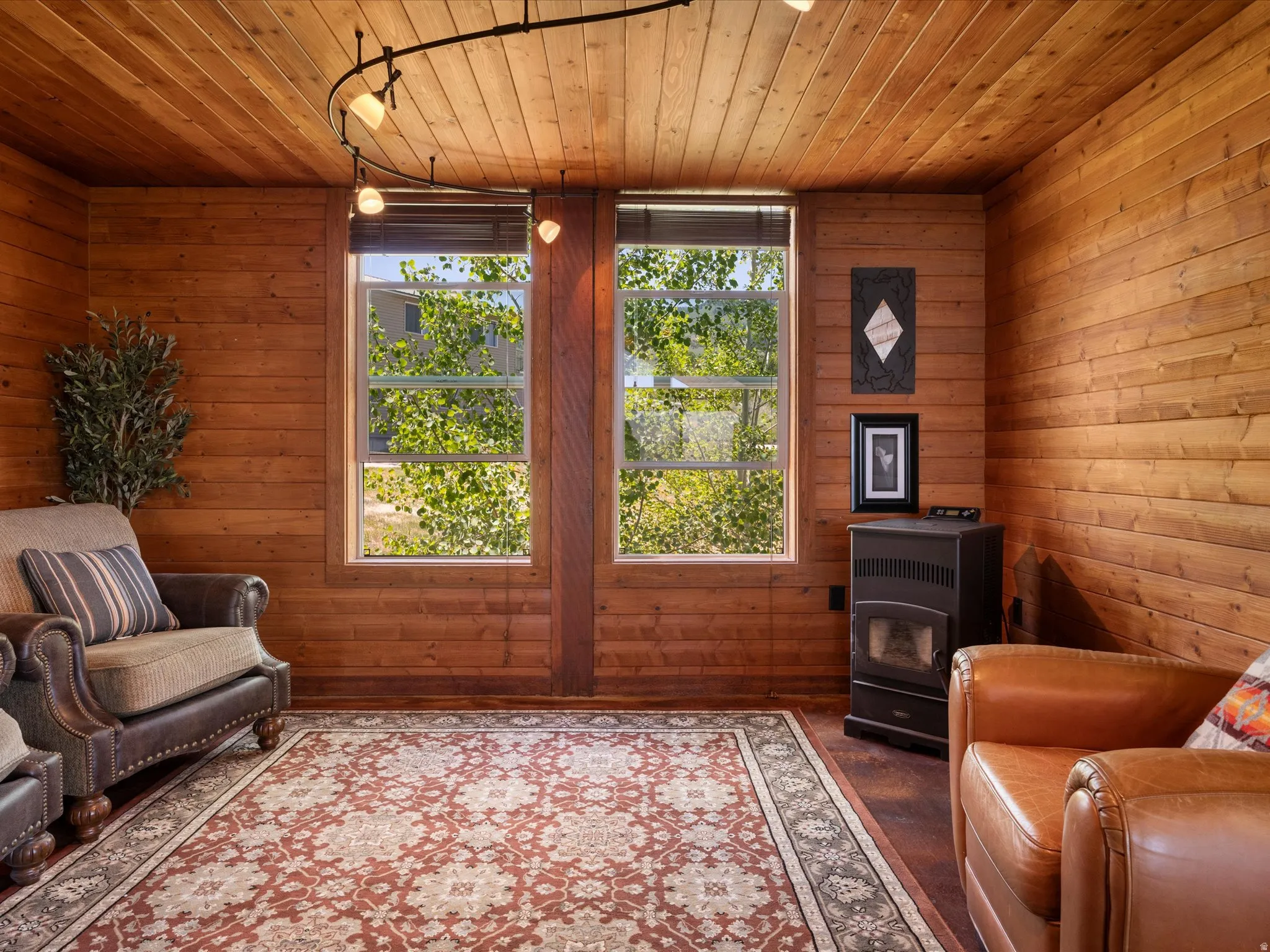 Wood-paneled room featuring a slatted wood ceiling, track lighting, two windows with blinds, a corner-placed stove, and a patterned area rug
