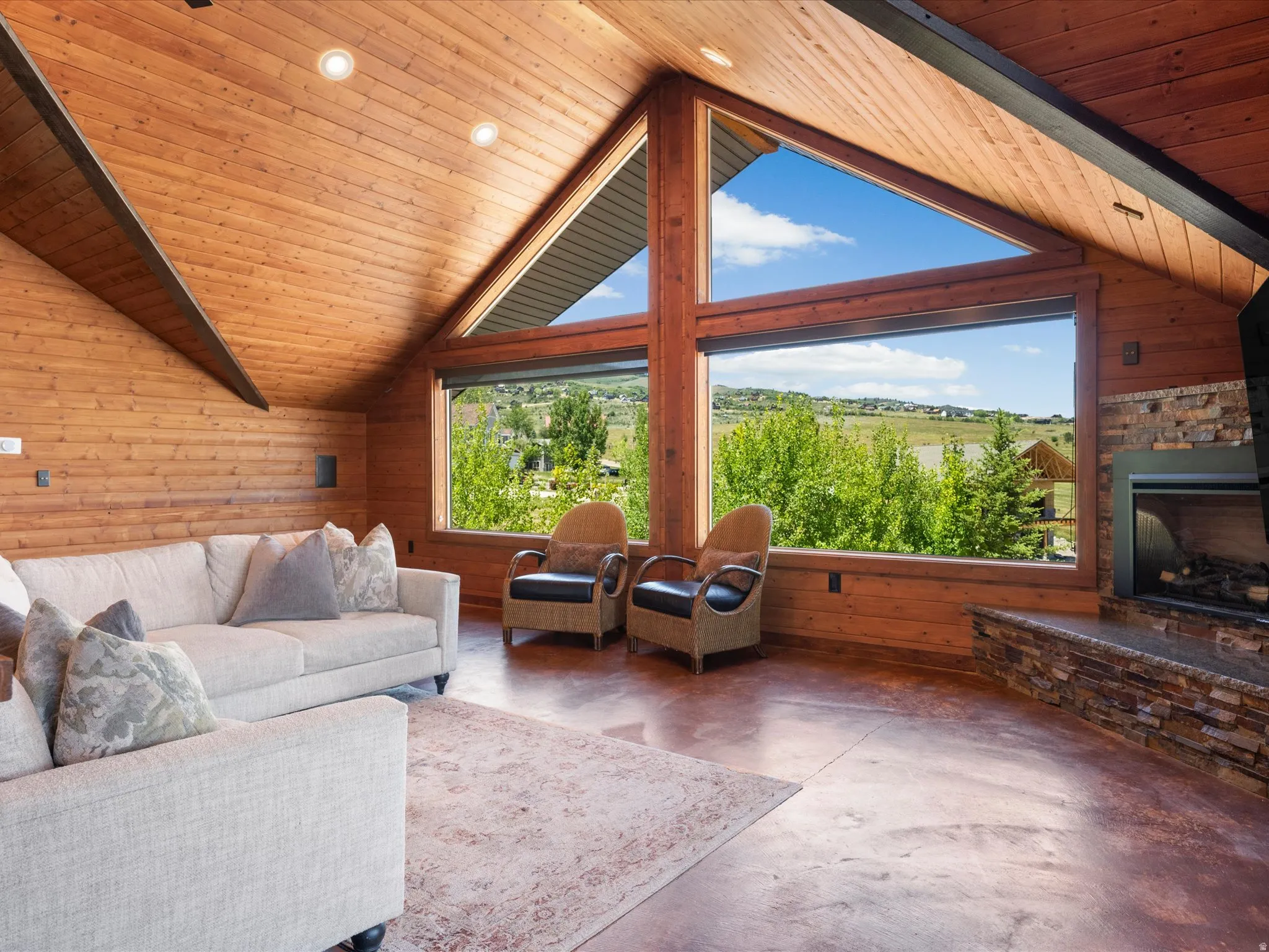 Vaulted wood-paneled ceilings with recessed lighting, floor-to-ceiling windows, and a stone-clad fireplace
