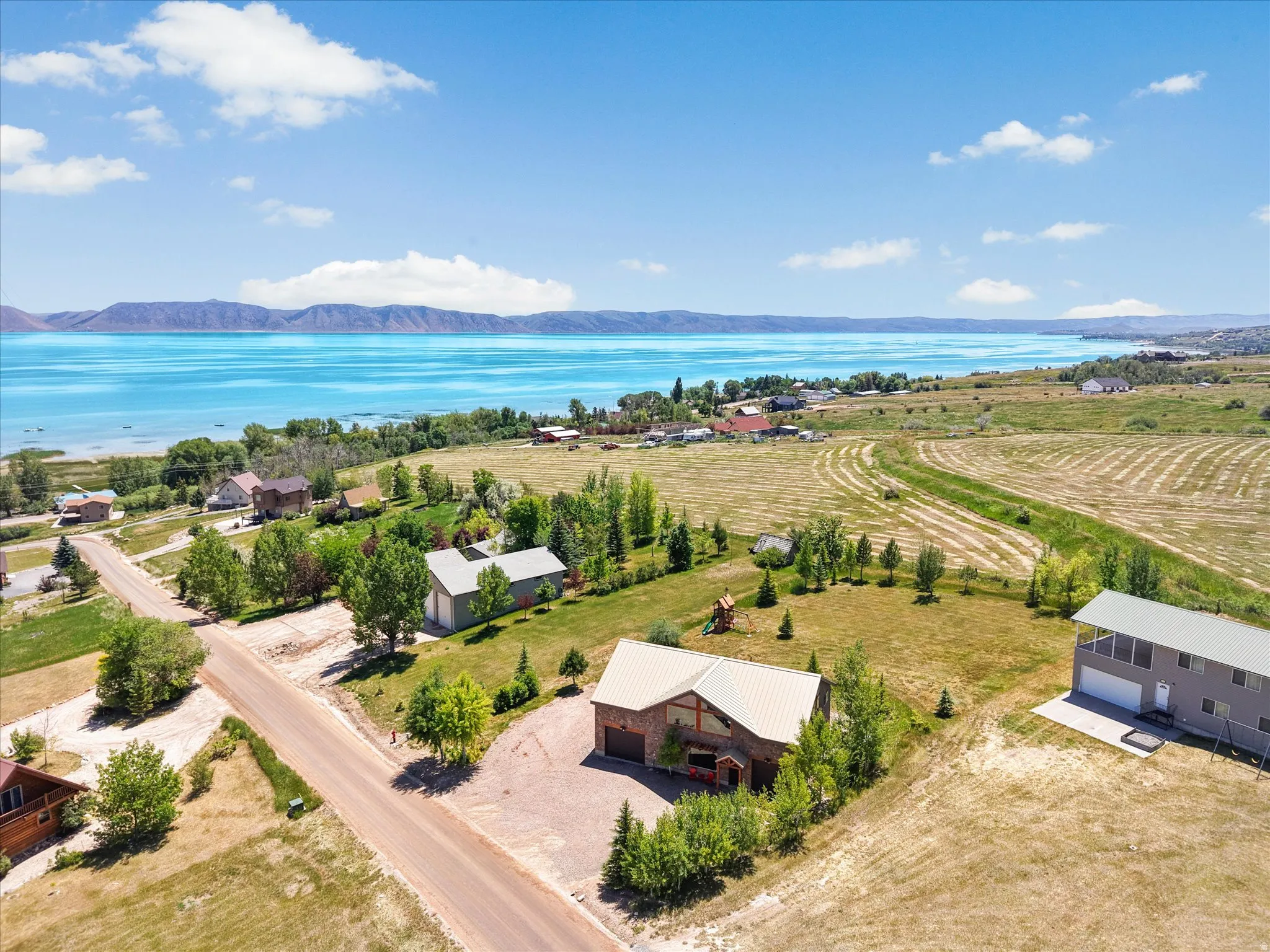 Expansive property with a metal-roofed residence and detached garage, featuring a gravel driveway and mature landscaping