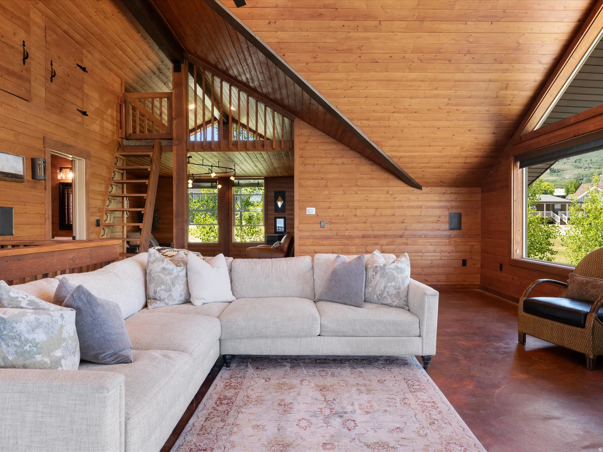 Expansive living area featuring vaulted wood-paneled ceilings, rich wood-finish walls, and a visible loft space with a ladder access