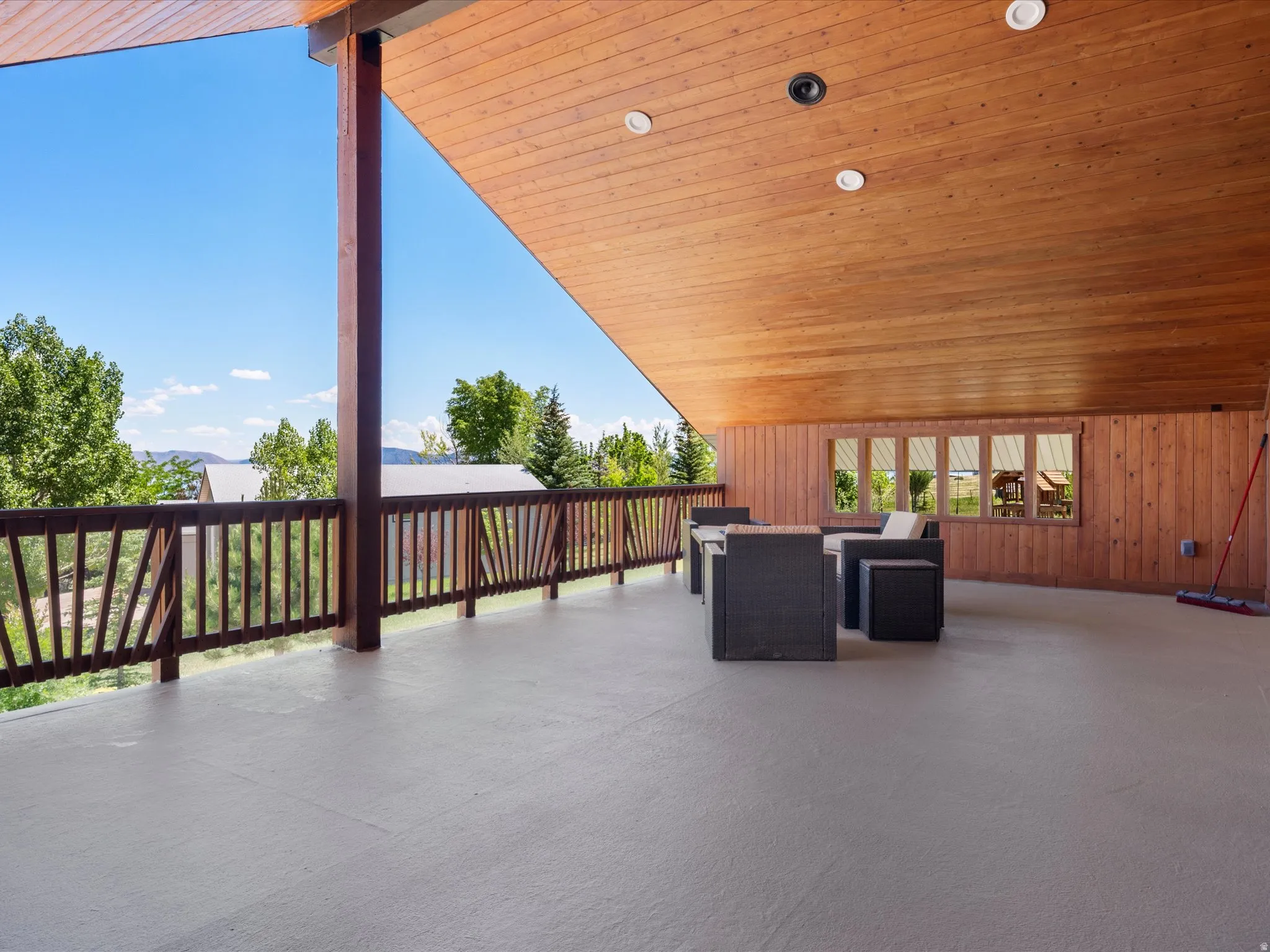 Spacious covered deck featuring a wood-panel ceiling, recessed lighting, and a wood railing with vertical balusters