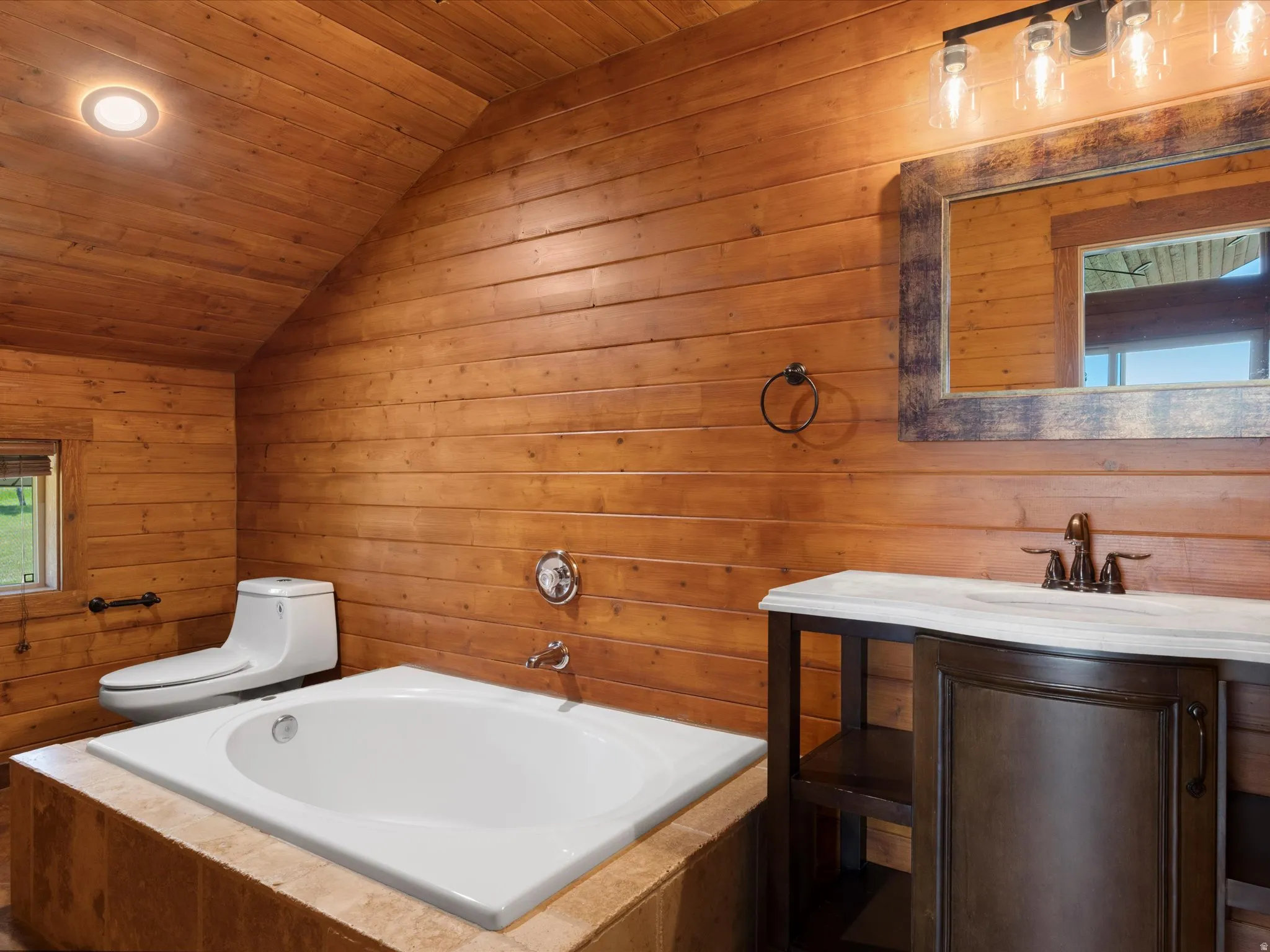 Bathroom featuring wood-paneled walls and ceiling, a built-in soaking tub with a tiled surround, a contemporary toilet, and a vanity with a white countertop and dark wood-finish cabinetry
