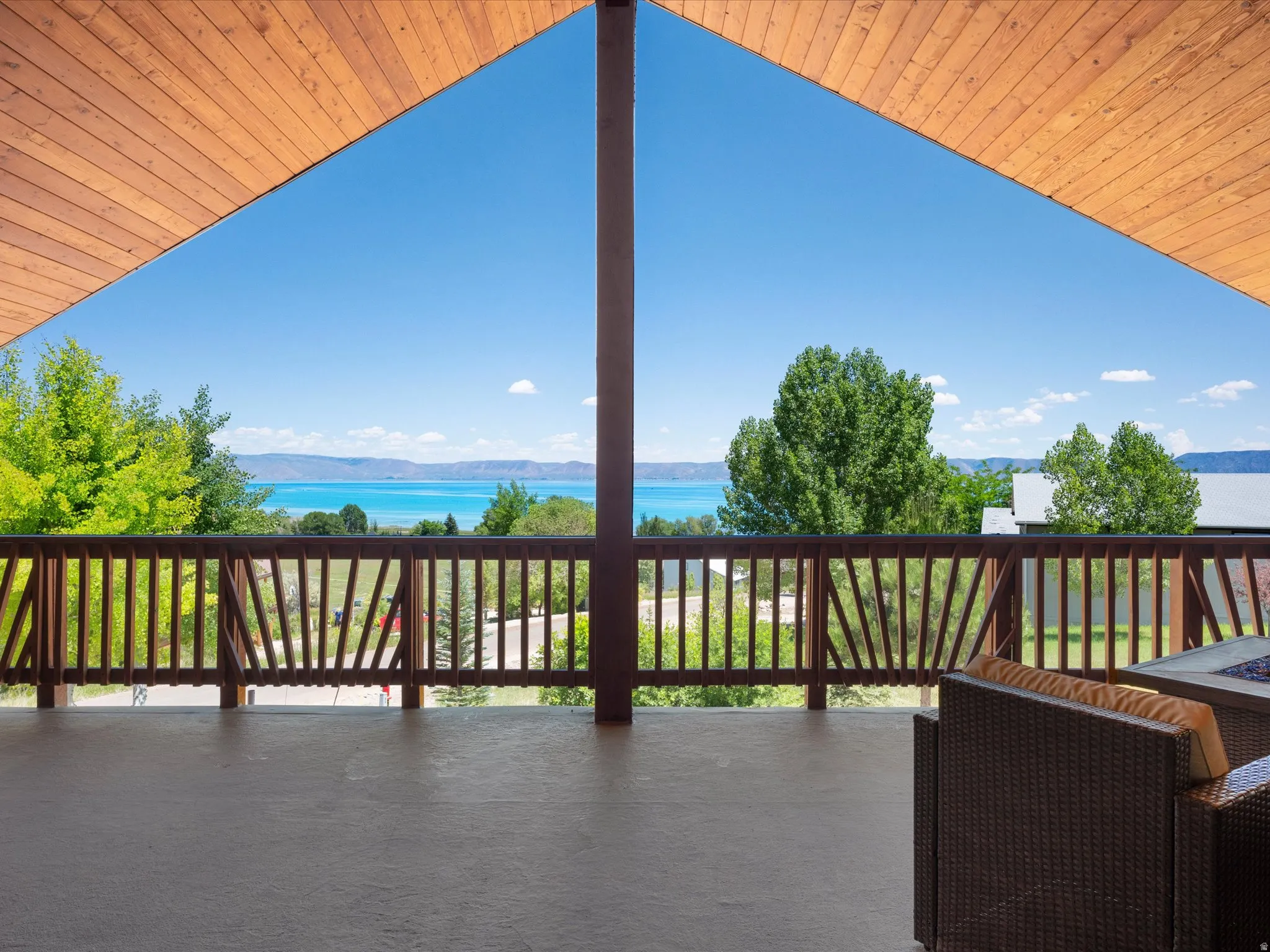 Expansive covered deck featuring a textured floor, slatted wood railing, and a vaulted wood-plank ceiling