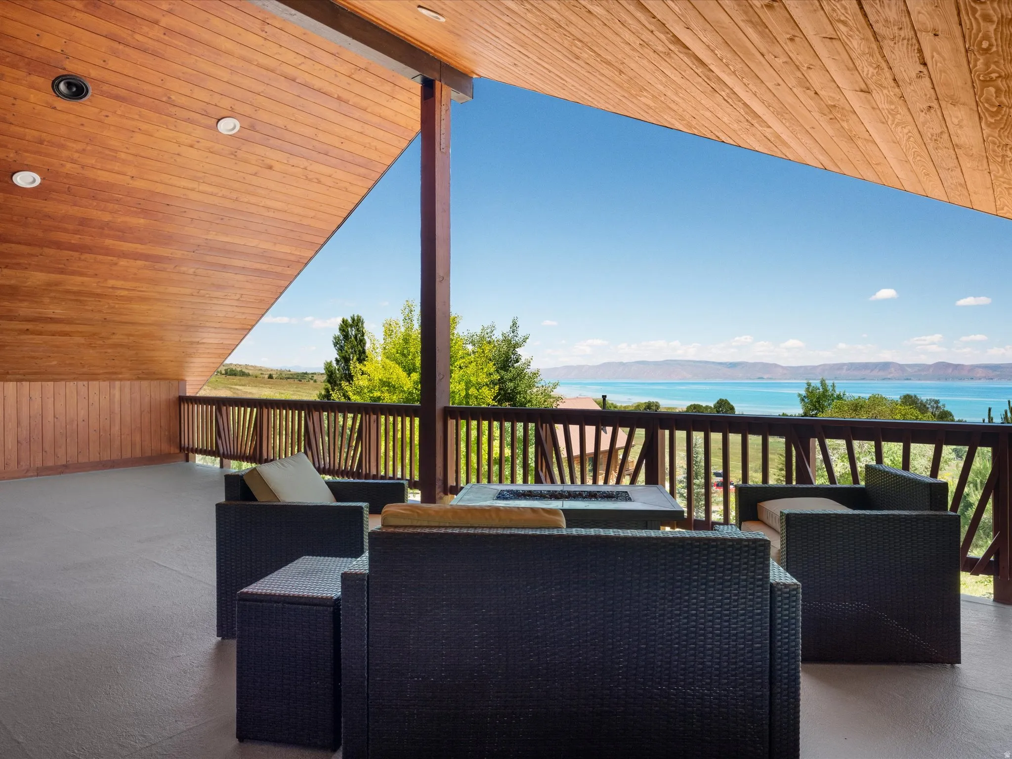 Covered outdoor deck with a horizontal wood-paneled ceiling, recessed lighting, and a wood railing