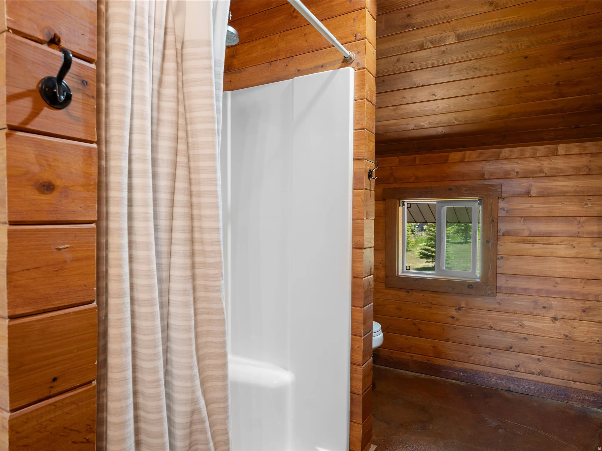 Shower enclosure with a white surround and chrome fixture, set against wood-paneled walls and a matching wood ceiling
