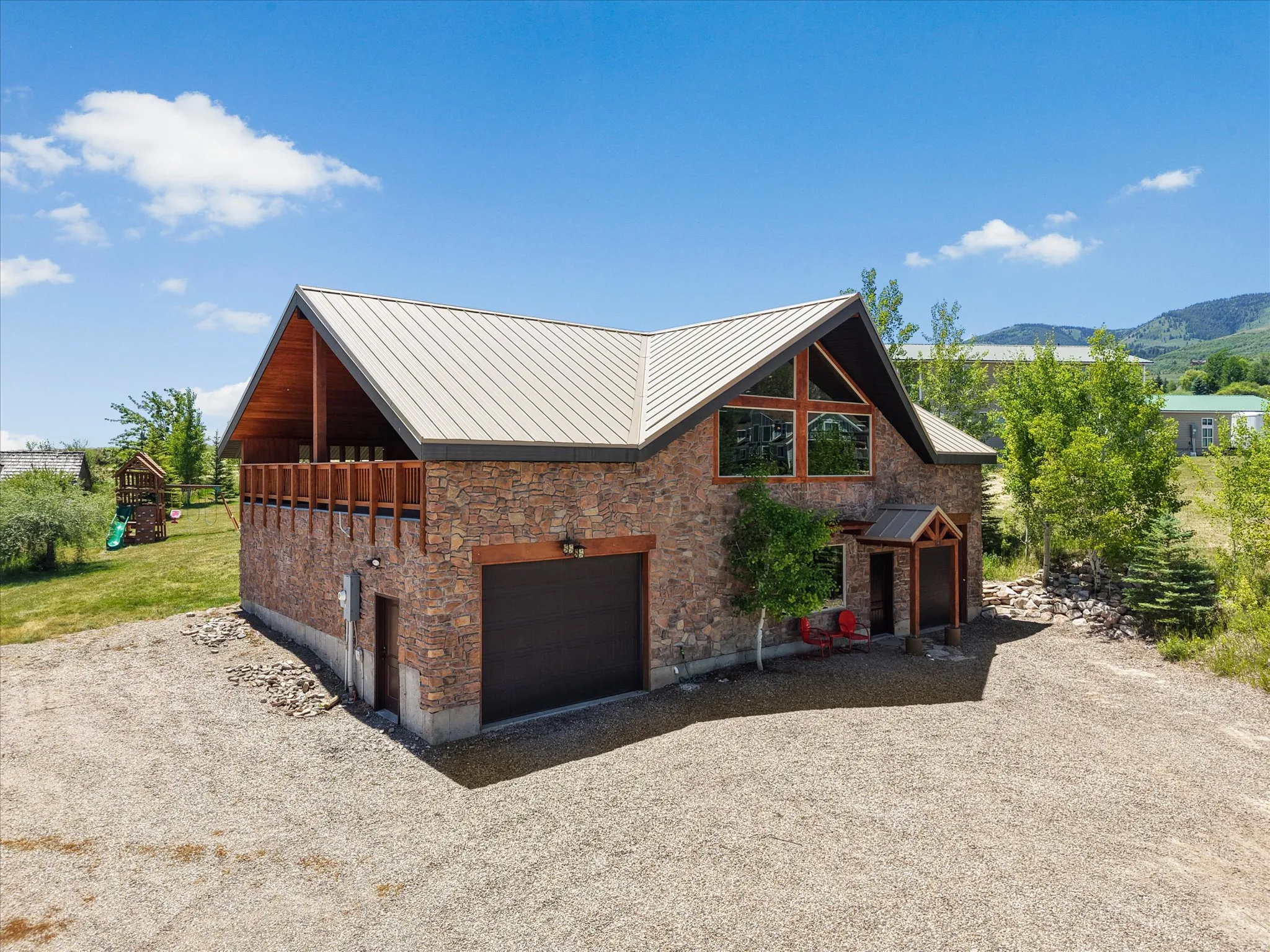 Stone facade structure featuring a metal roof, an integrated garage, an upper-level balcony with wood railing, and a prominent front entrance with a covered porch