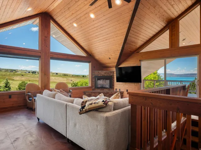 Vaulted wood-paneled ceilings with recessed lighting, floor-to-ceiling windows, a stone-faced fireplace, a sliding glass door, and wood railings
