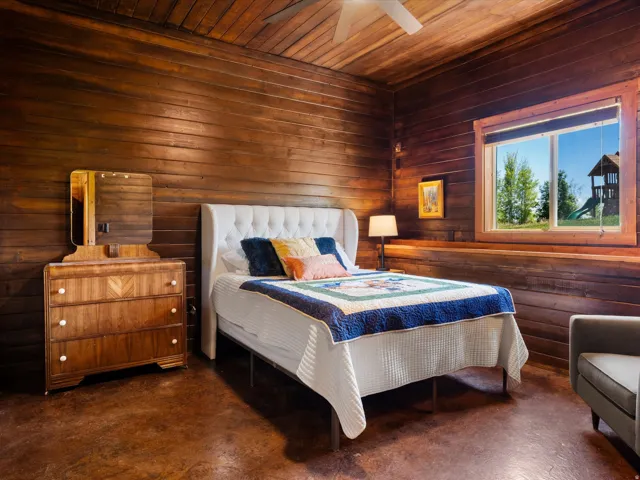Interior space featuring wood-paneled walls and ceiling, a large window with wood trim, and textured flooring