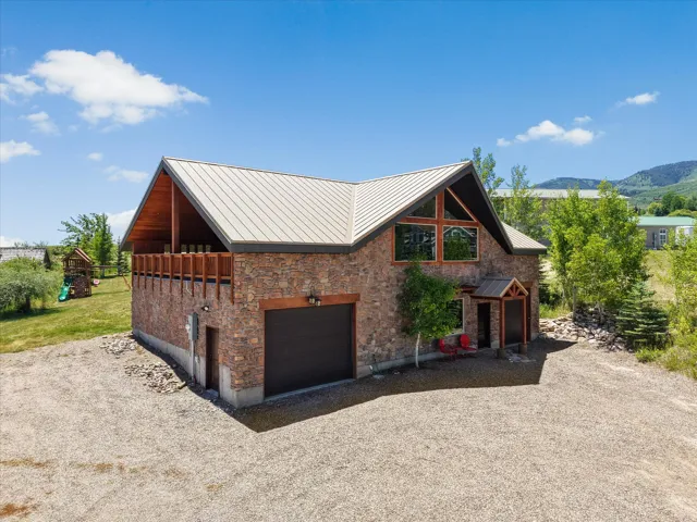Stone facade structure featuring a metal roof, an integrated garage, an upper-level balcony with wood railing, and a prominent front entrance with a covered porch