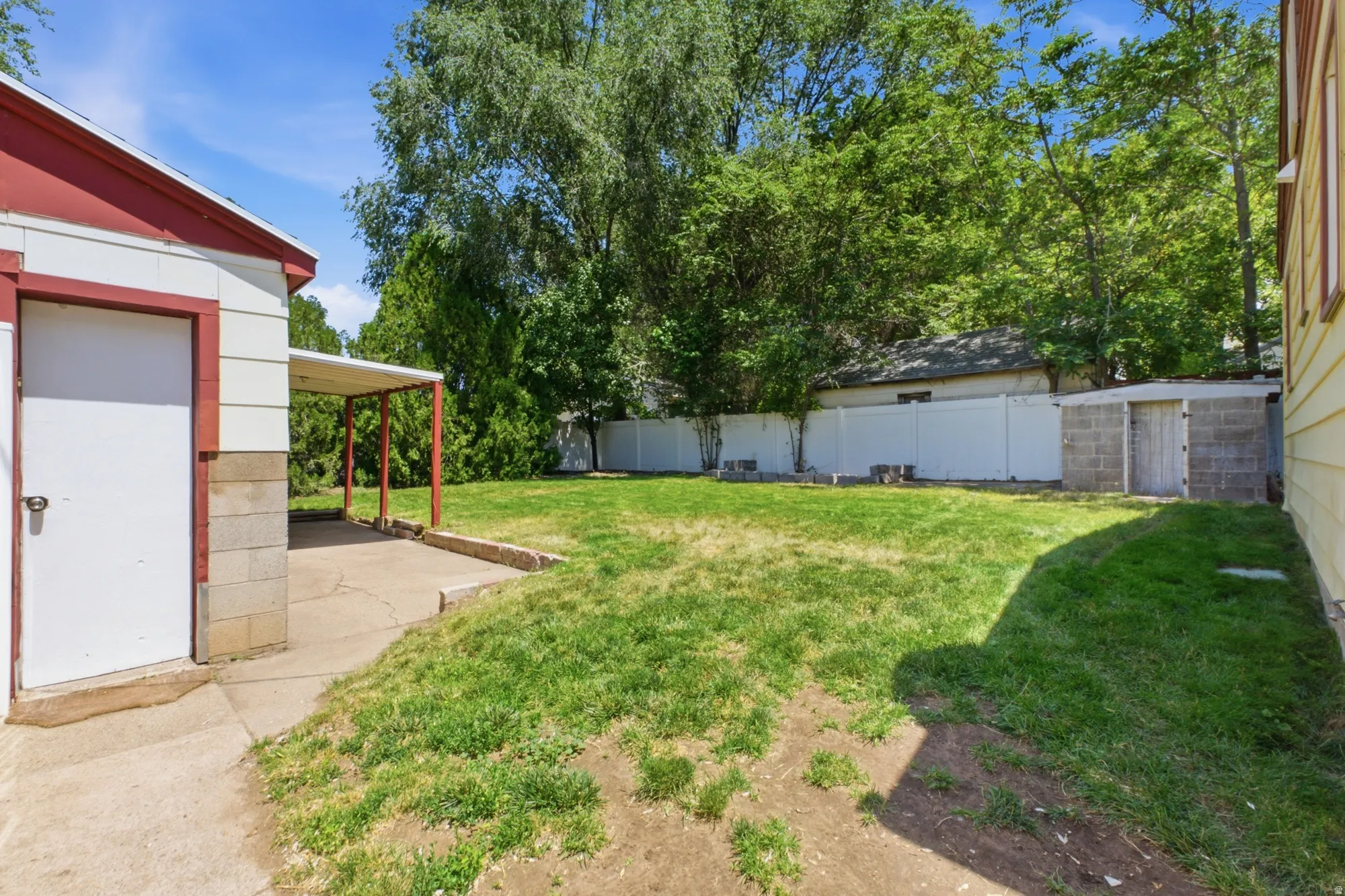 Fenced backyard with lawn space, mature trees, detached garage, and patio area.