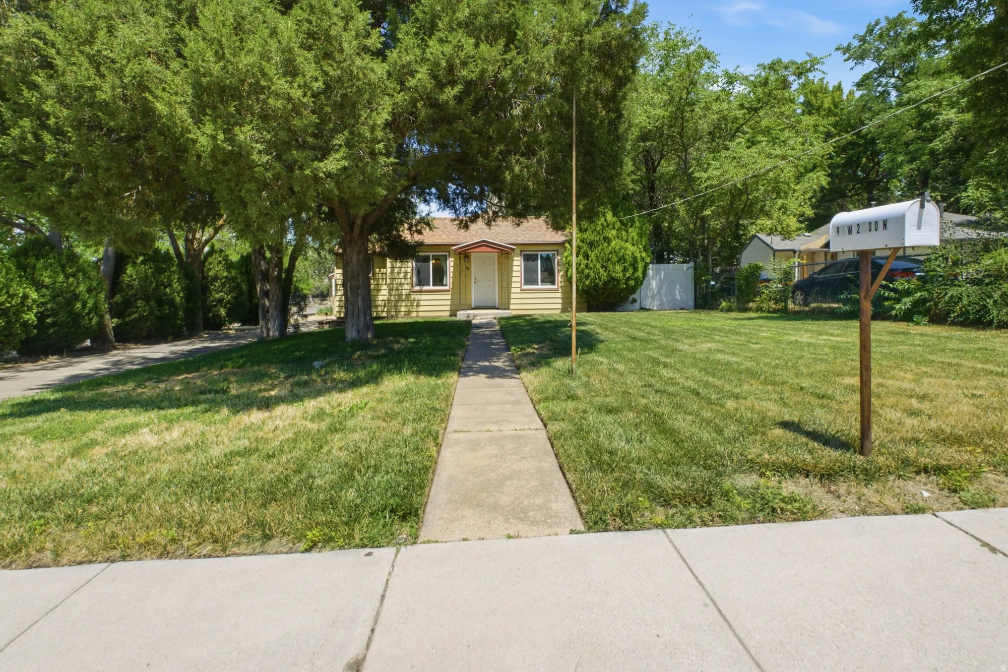 Wide front exterior view with mature trees, walkway to the home, lawn space, and established neighborhood setting.
