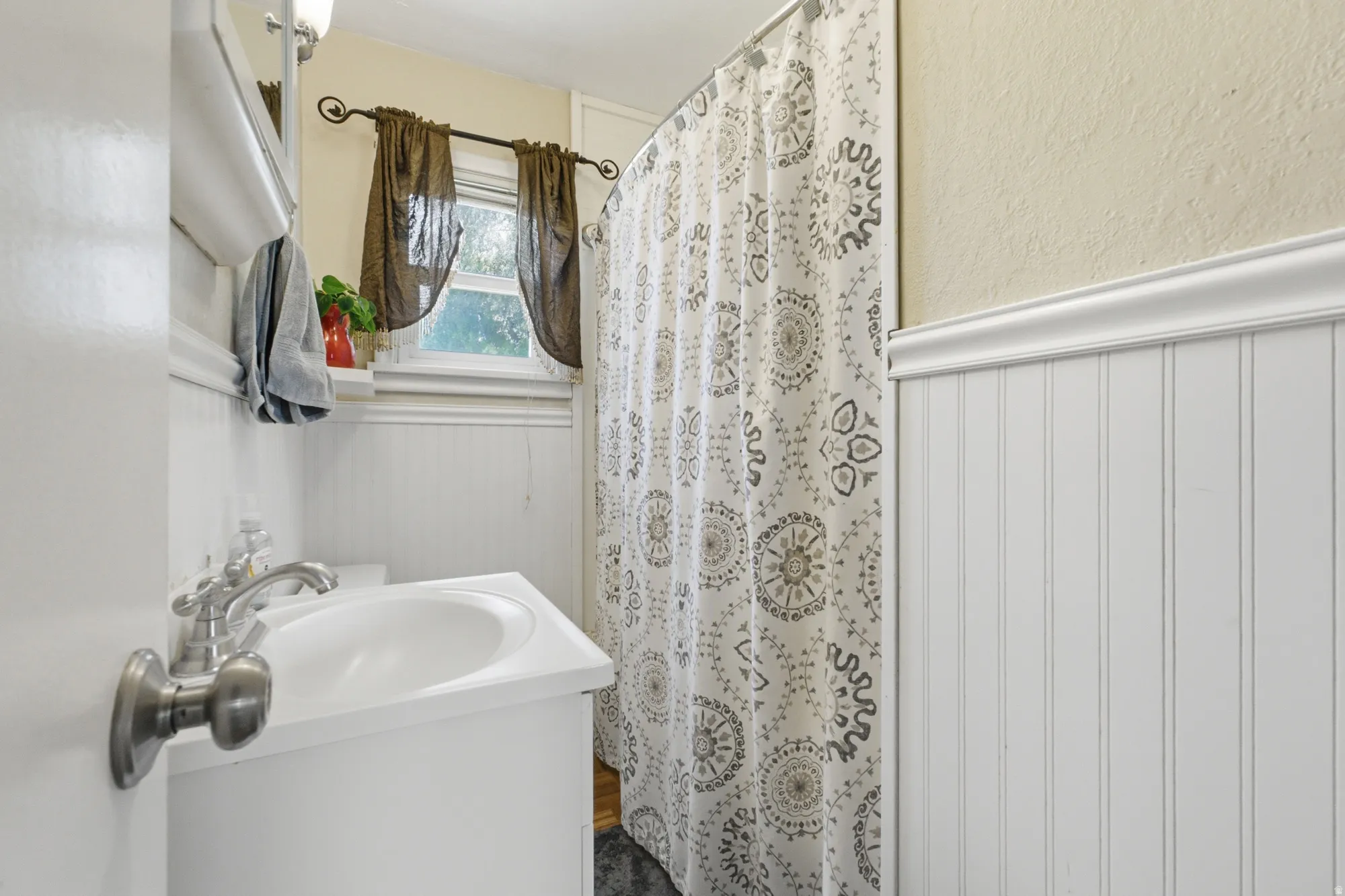 Bathroom featuring white beadboard paneling, a single vanity with an integrated sink, and an overhead light fixture, window for natural light, and shower/tub combination.