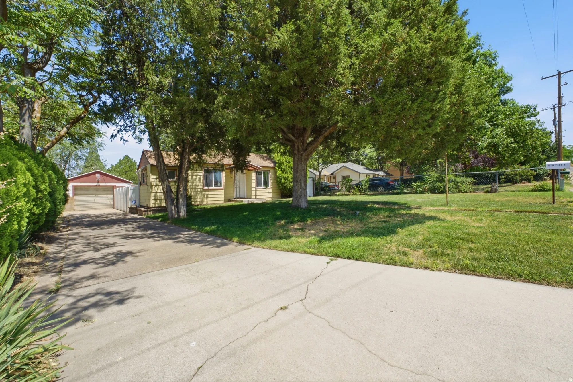 Wide exterior view featuring mature trees, long driveway, detached garage, and spacious front yard with established landscaping.