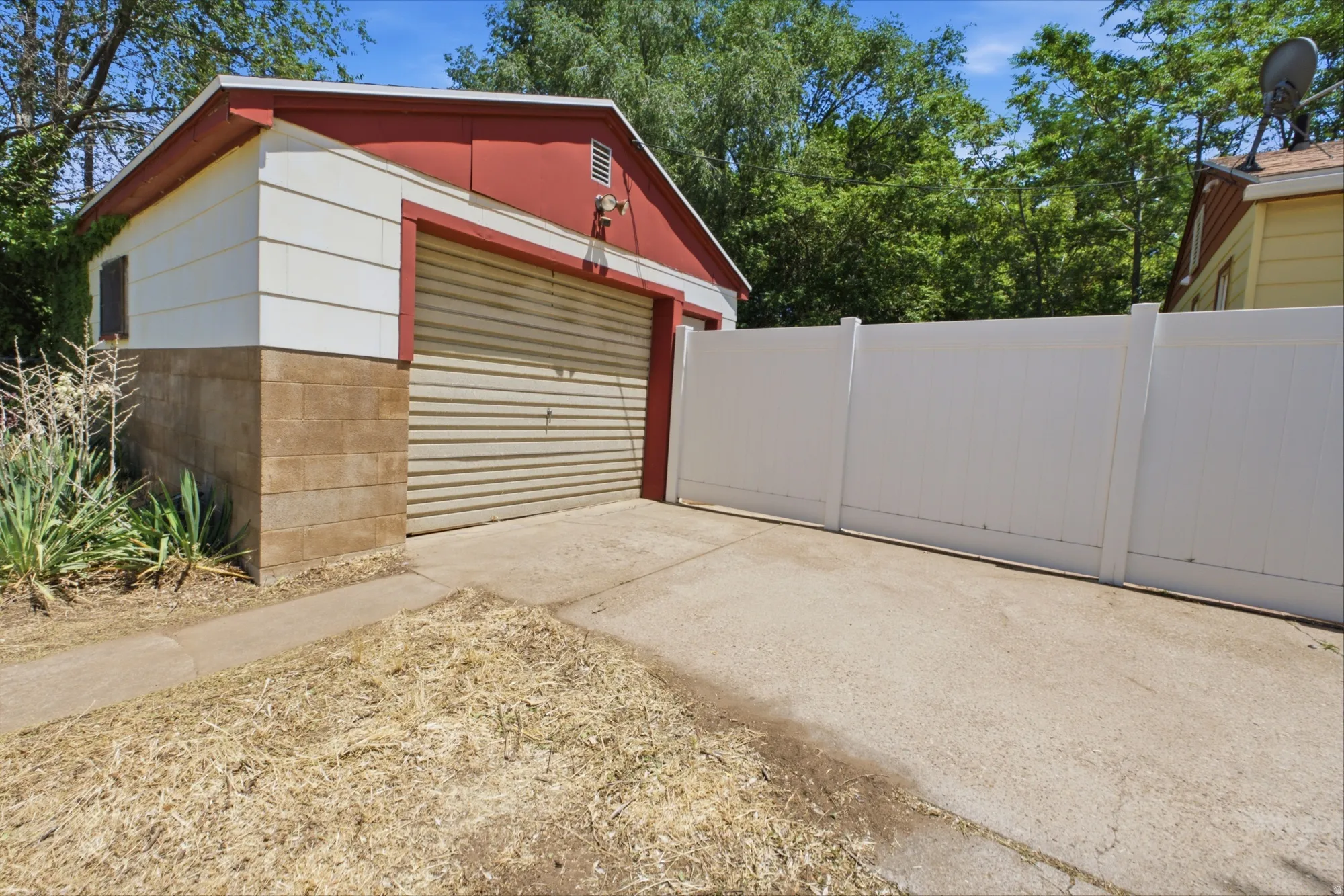 Detached garage with roll-up door, concrete driveway, and enclosed yard access.