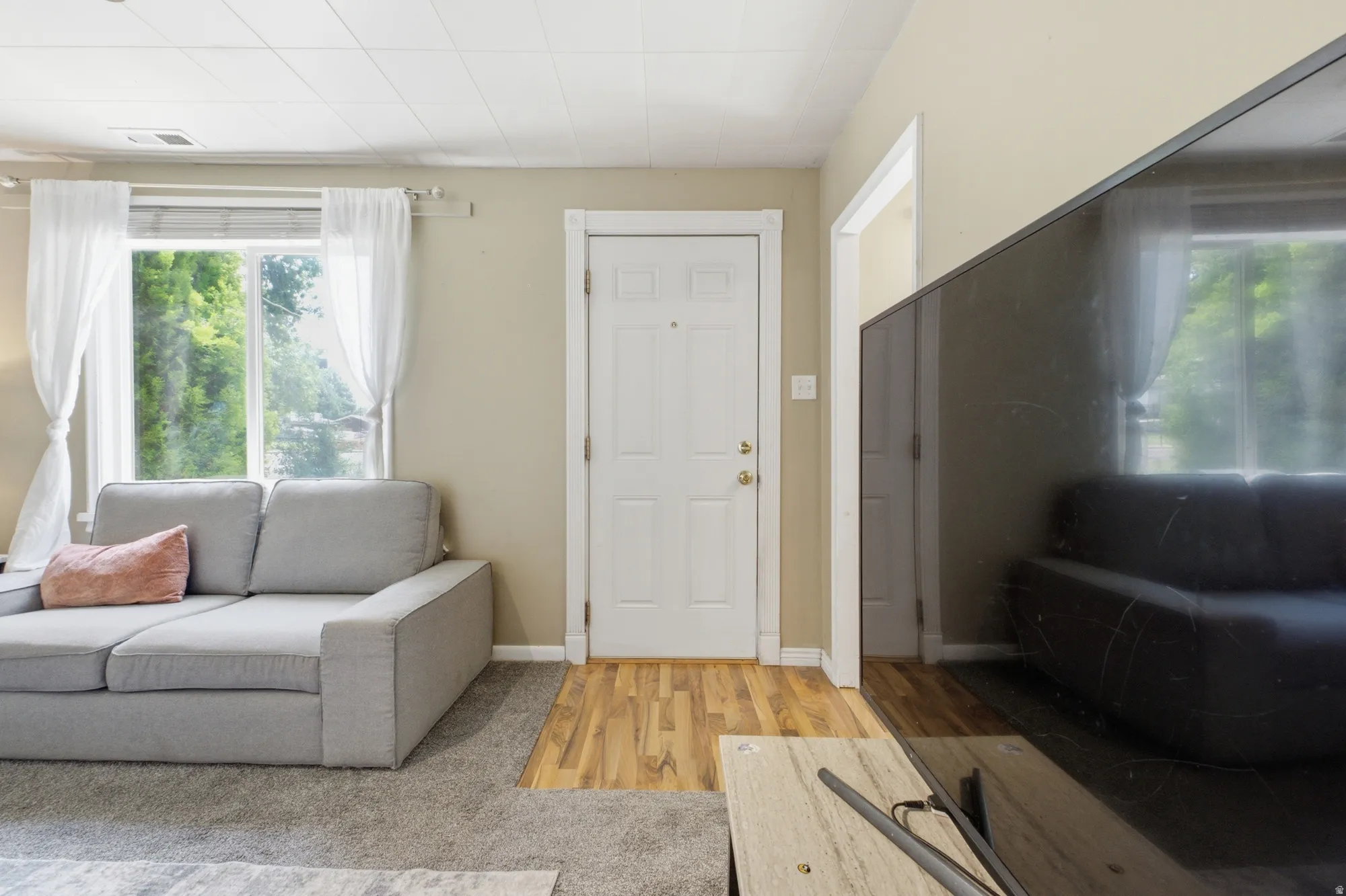 Comfortable living room with front door access, large window, neutral tones, and a cozy layout.