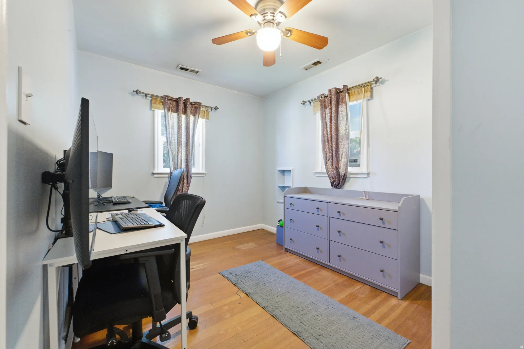 Flexible bedroom or office space with hardwood flooring, two windows, ceiling fan, and great natural light.
