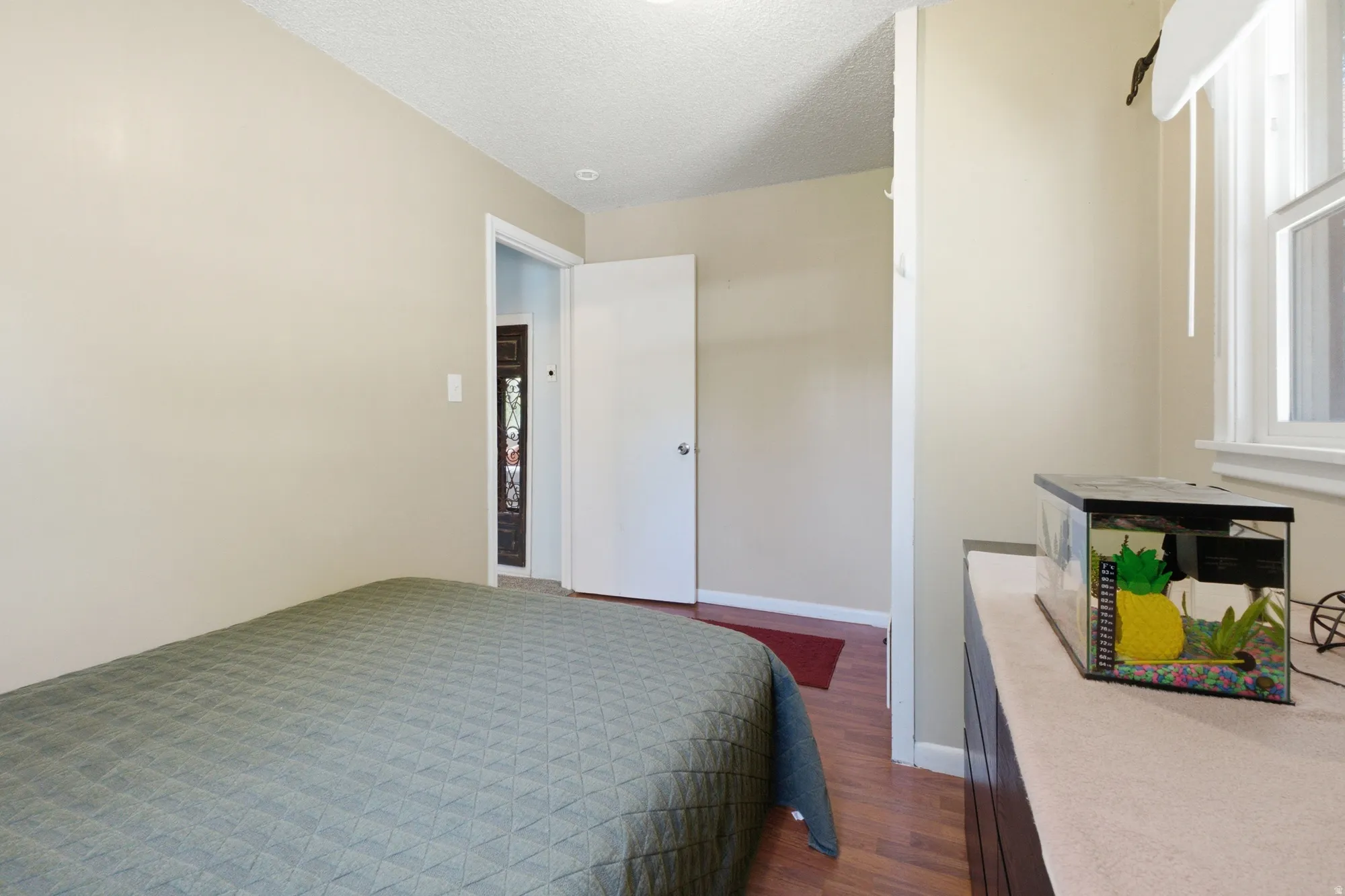 Bedroom with neutral walls, warm flooring, and natural light from the window.