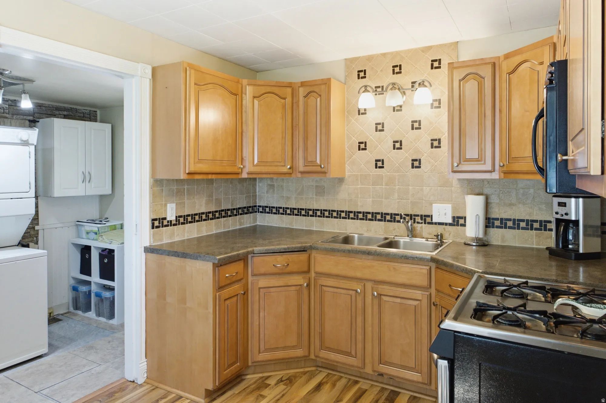 Kitchen featuring wood cabinetry, tile backsplash, gas range, and convenient access to the laundry/utility area.