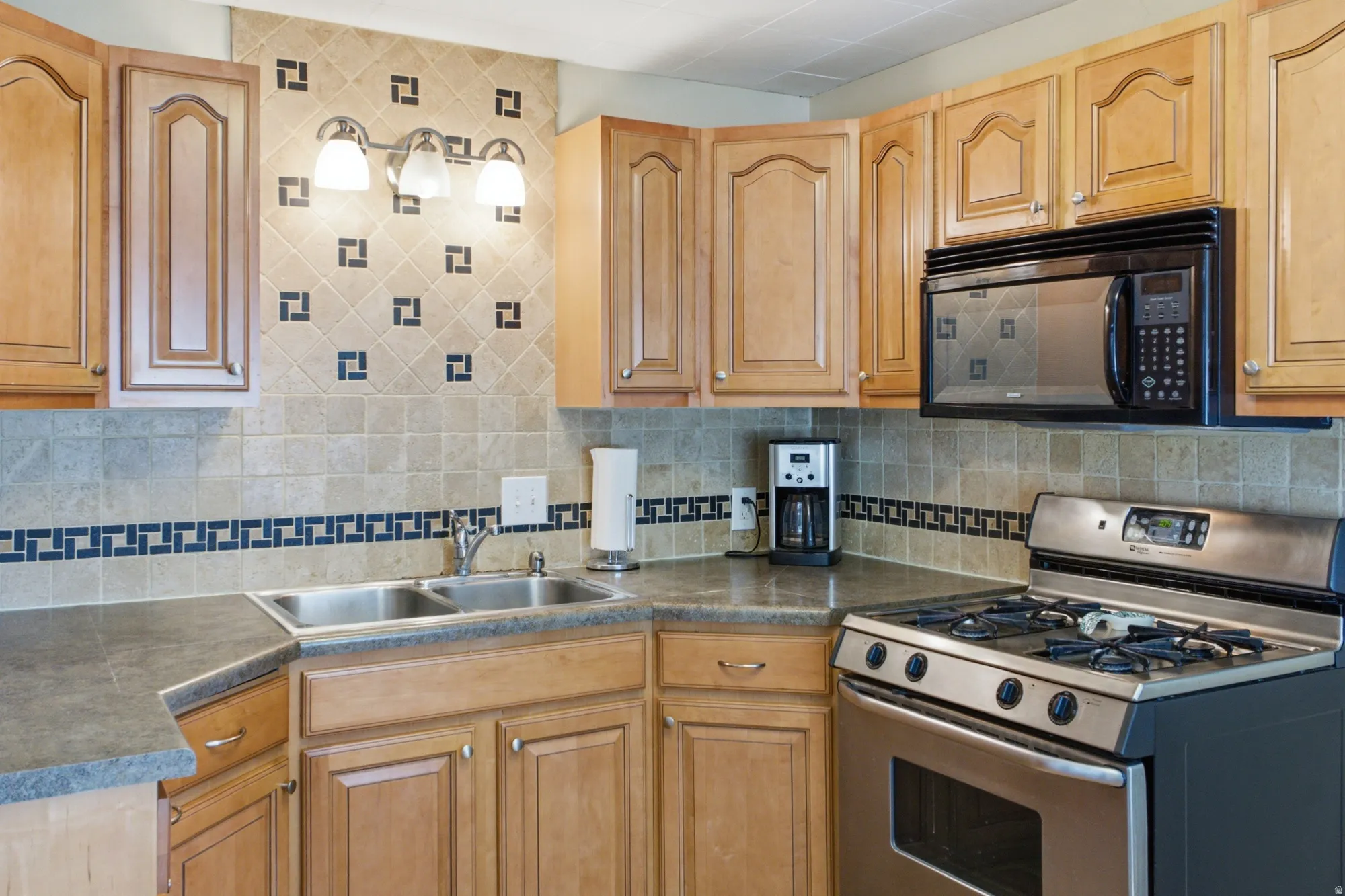 Detailed kitchen view highlighting the tile backsplash, cabinet storage, double sink, gas range, and built-in microwave.