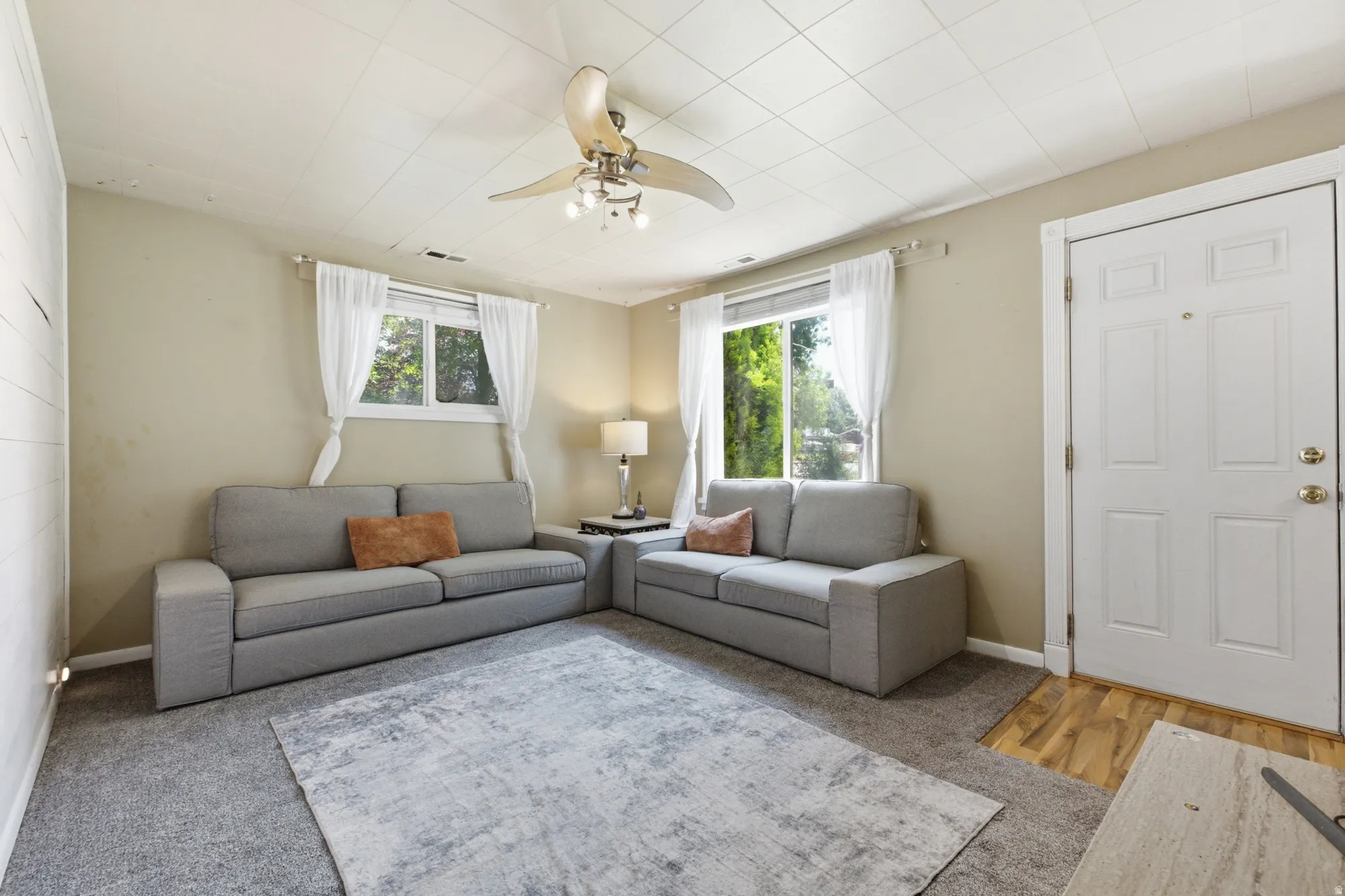 Bright living room featuring multiple windows, ceiling fan, soft carpet, and space for everyday relaxing or entertaining.