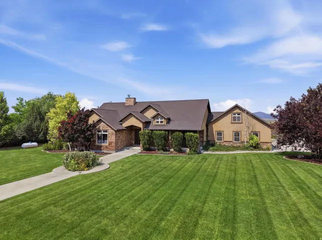 Spacious front yard with a stone and stucco exterior, dark shingle roof, mature landscaping, and an extended concrete driveway