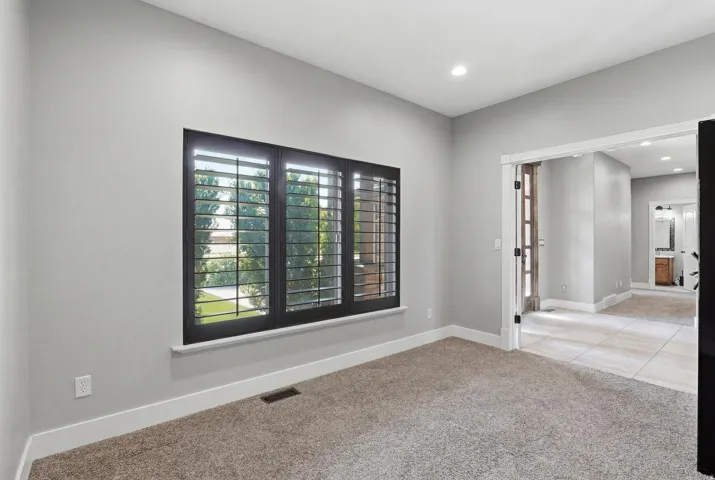 Interior room featuring a large window with dark plantation shutters, light gray walls, and plush carpeting
