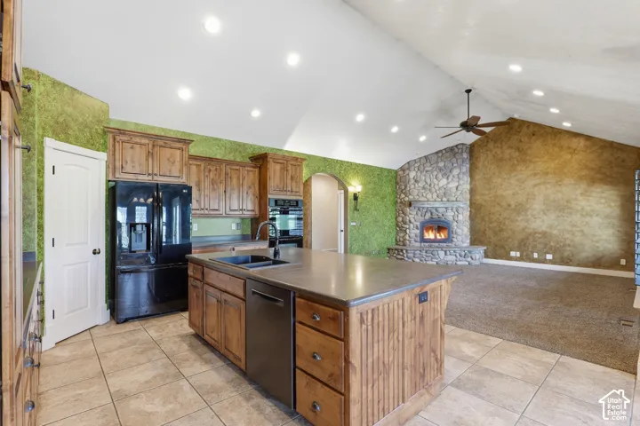 Open-concept kitchen and living area featuring a stone fireplace, vaulted ceilings with recessed lighting and a ceiling fan, and a kitchen island with integrated sink and dishwasher