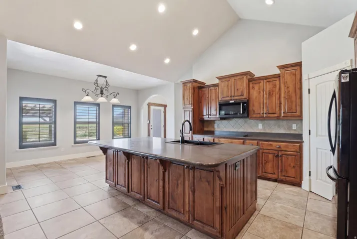 Kitchen featuring a large island with integrated sink, wood cabinetry, tile flooring, and a vaulted ceiling