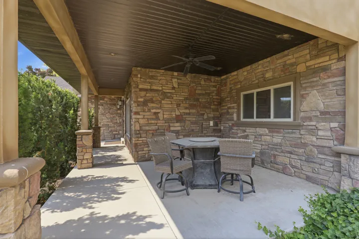 Covered patio featuring stone veneer walls, a corrugated metal ceiling, and a ceiling fan
